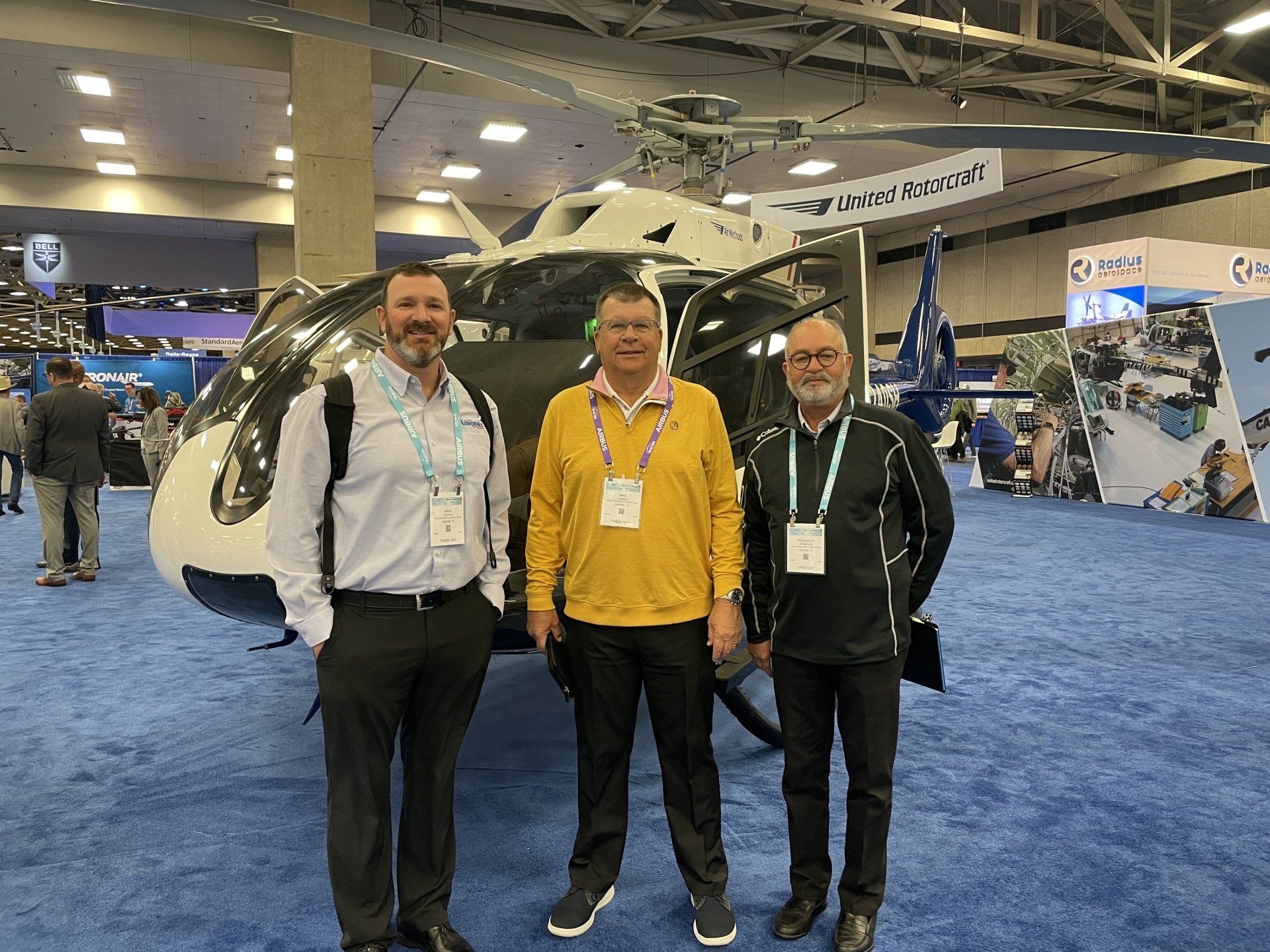 Three men are posing for a picture in front of a helicopter.
