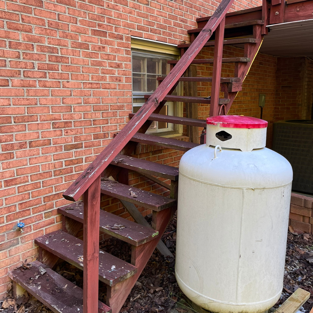 A propane tank is sitting next to a set of stairs.