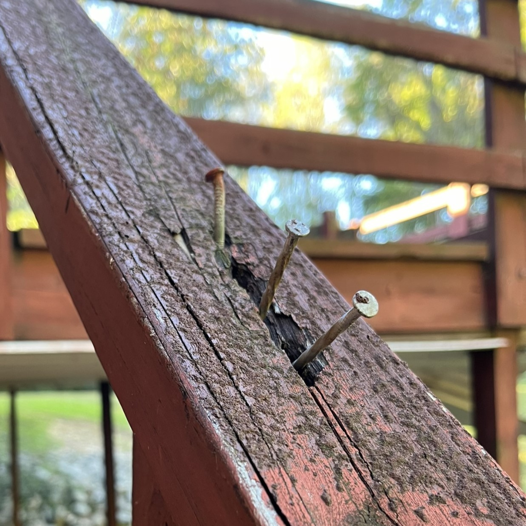 A wooden railing with nails sticking out of it.