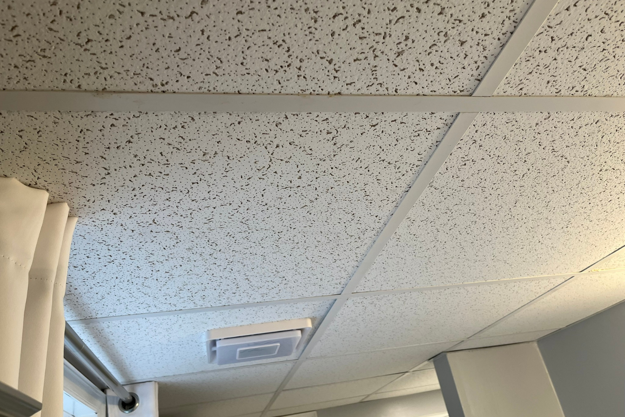 A white tiled ceiling in a room with a window.