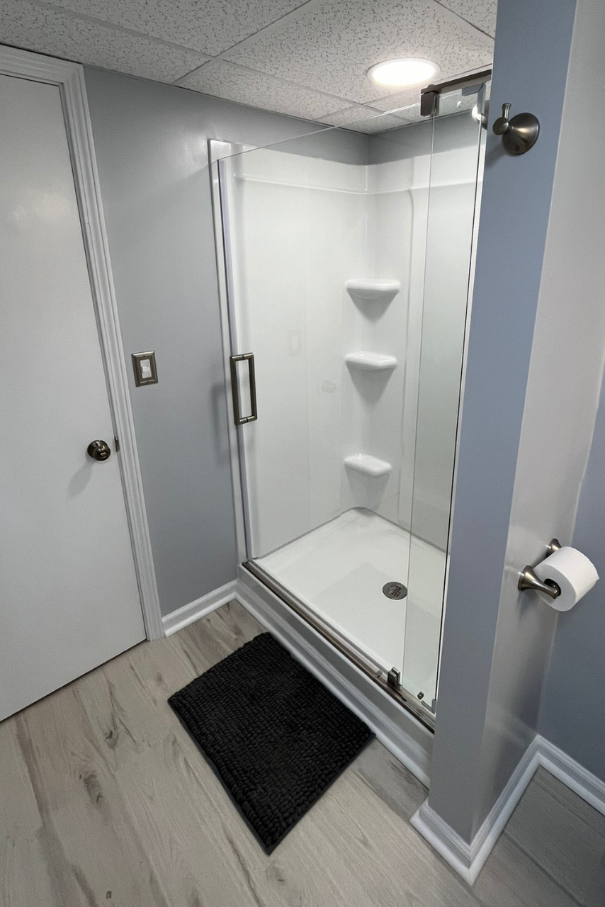 A bathroom with a walk in shower and a black mat on the floor.