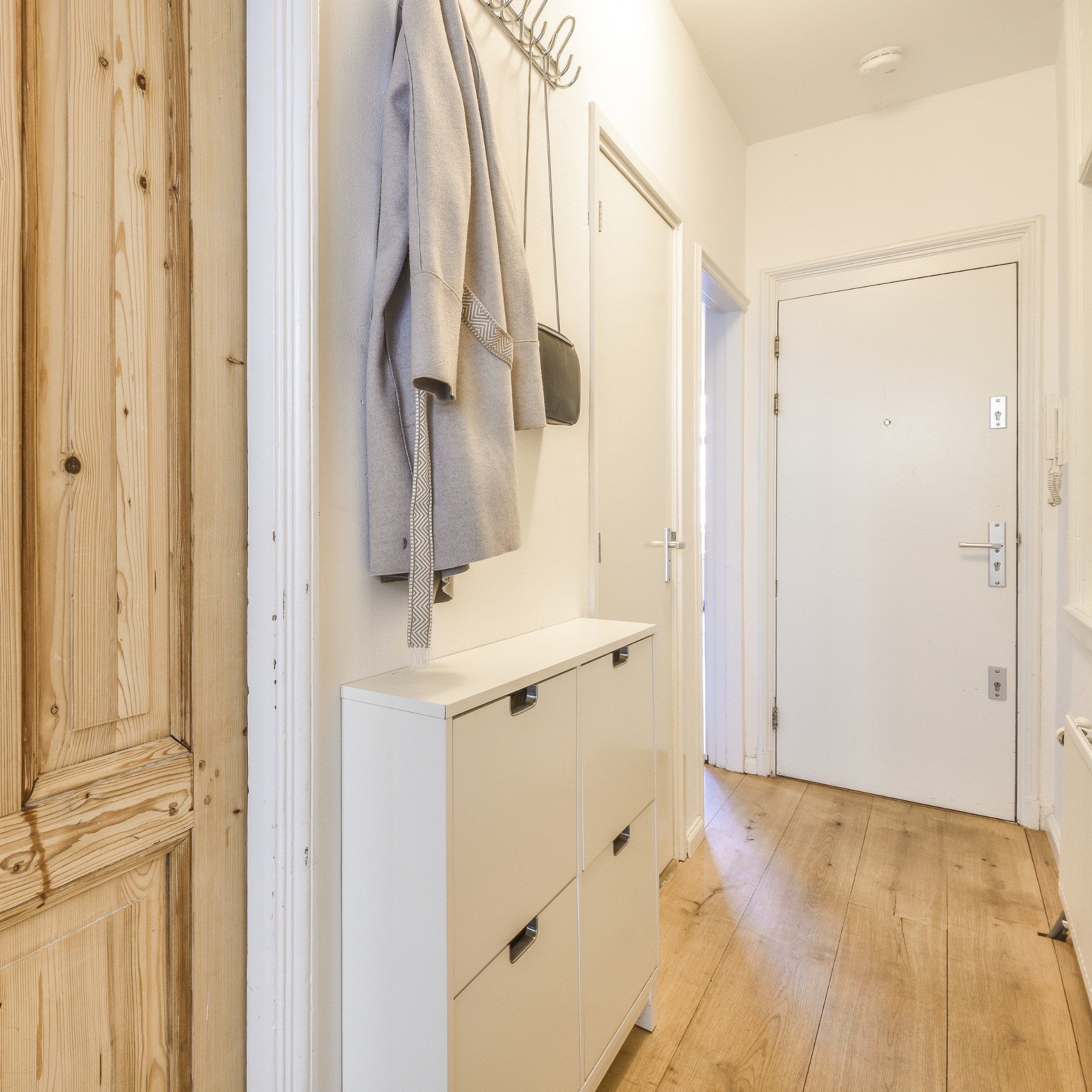 A hallway with a coat hanging on the wall and a shoe rack