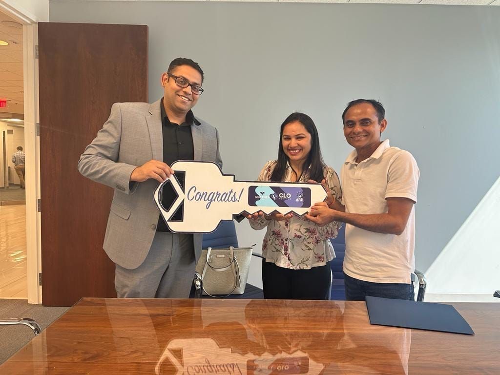 Three people smiling and holding a “Congrats!” sign in a conference room
