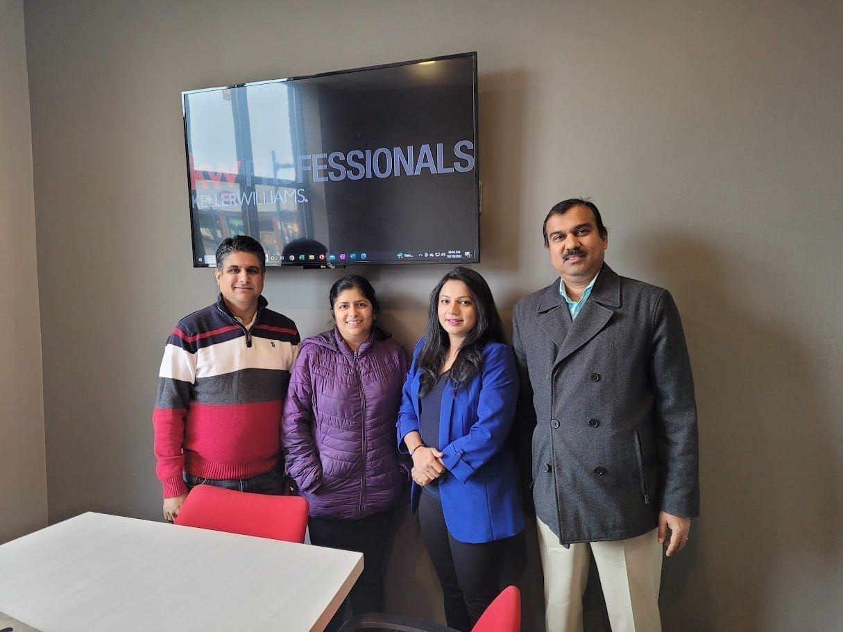 Four people posing in an office beside a wall-mounted screen displaying “PROFESSIONALS.”