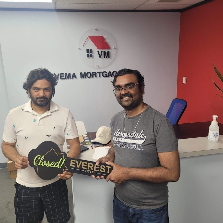 Two men holding a “Closed” sign and “EVEREST” letters in an office with Yema Mortgage branding