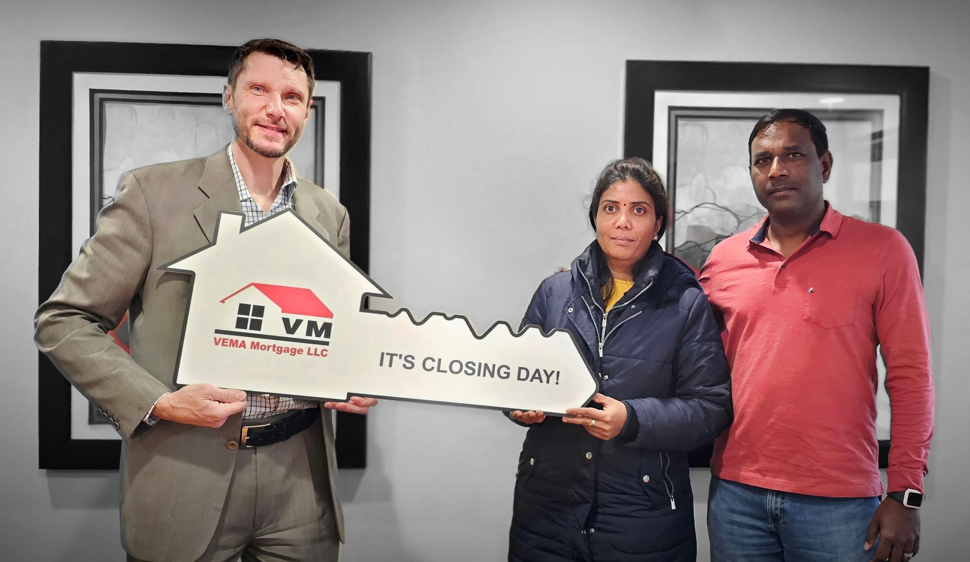 Three people hold a large key-shaped plaque in an office, with one man smiling beside two others.