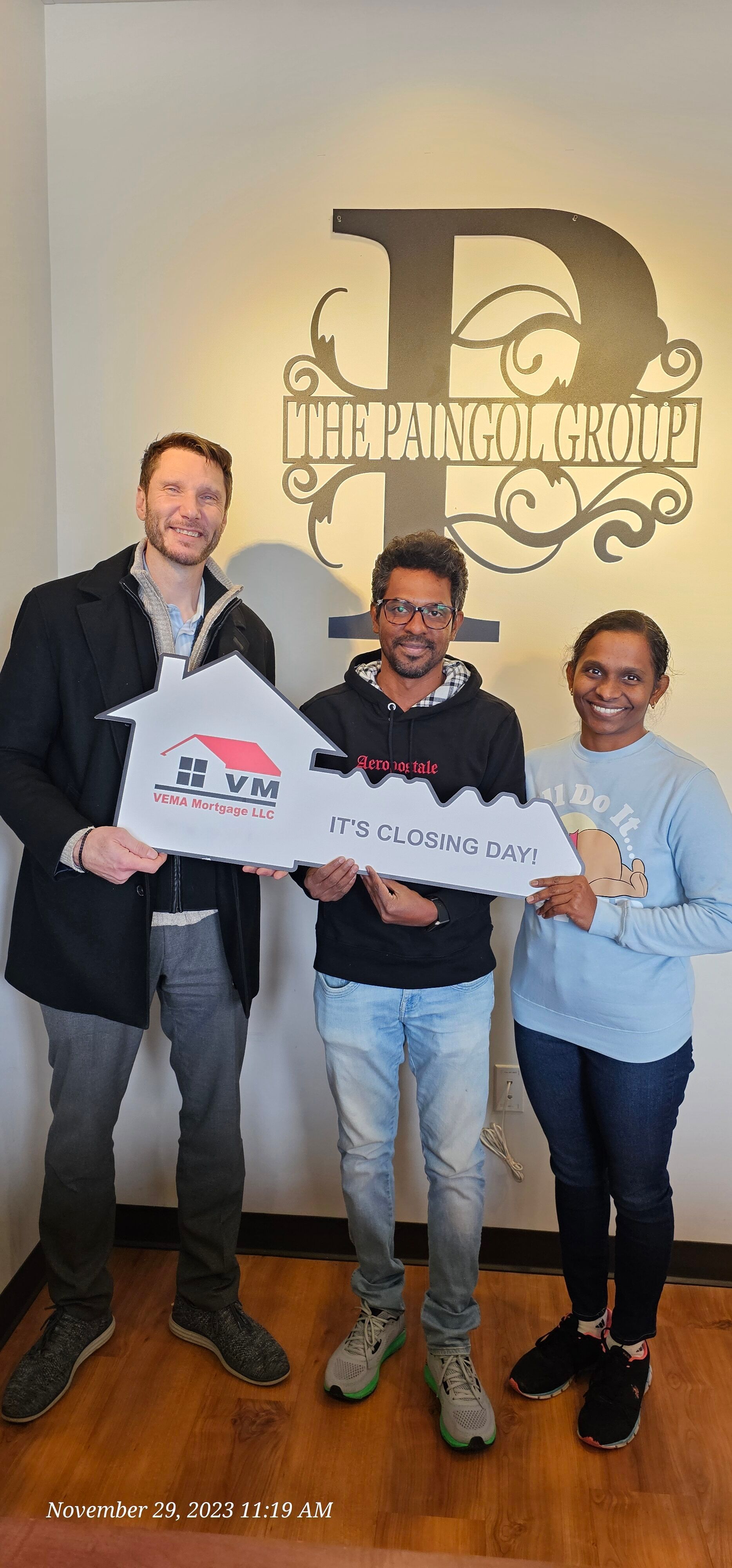Three smiling people holding signs in front of a large wall logo indoors