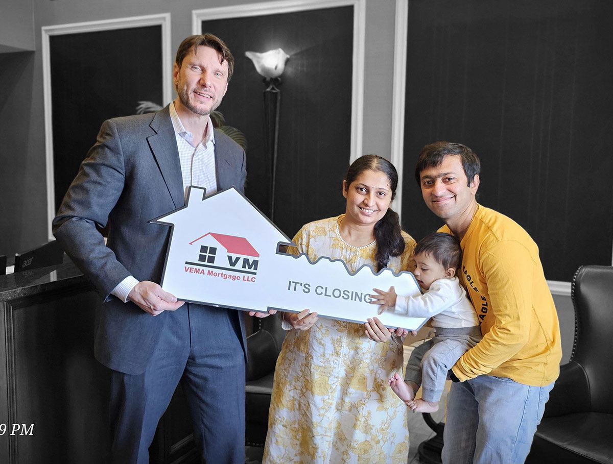 Four people pose indoors holding a sign, with smiling expressions in a dark-walled room.