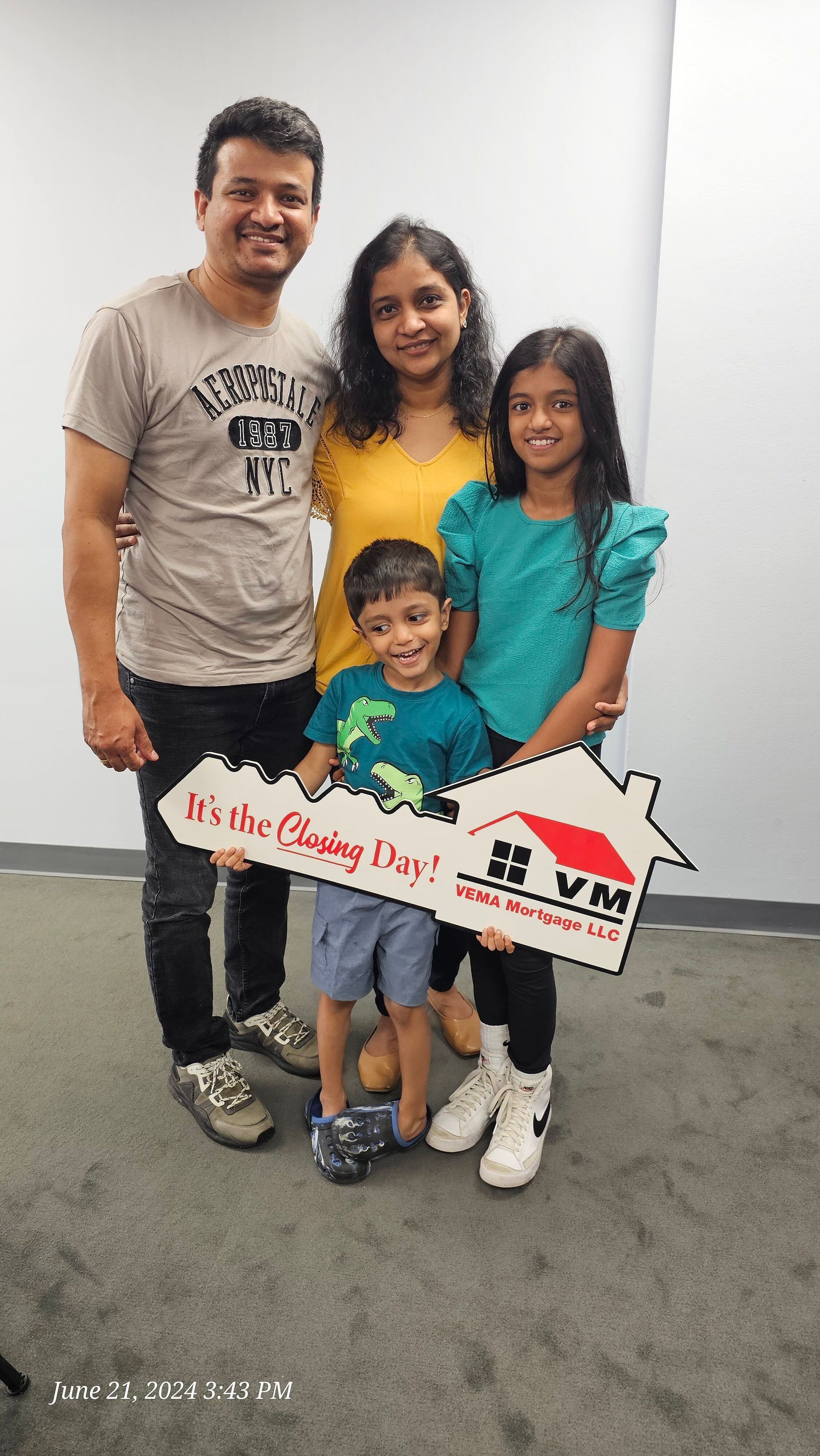 Family of four posing indoors with a sign, smiling and standing close together.