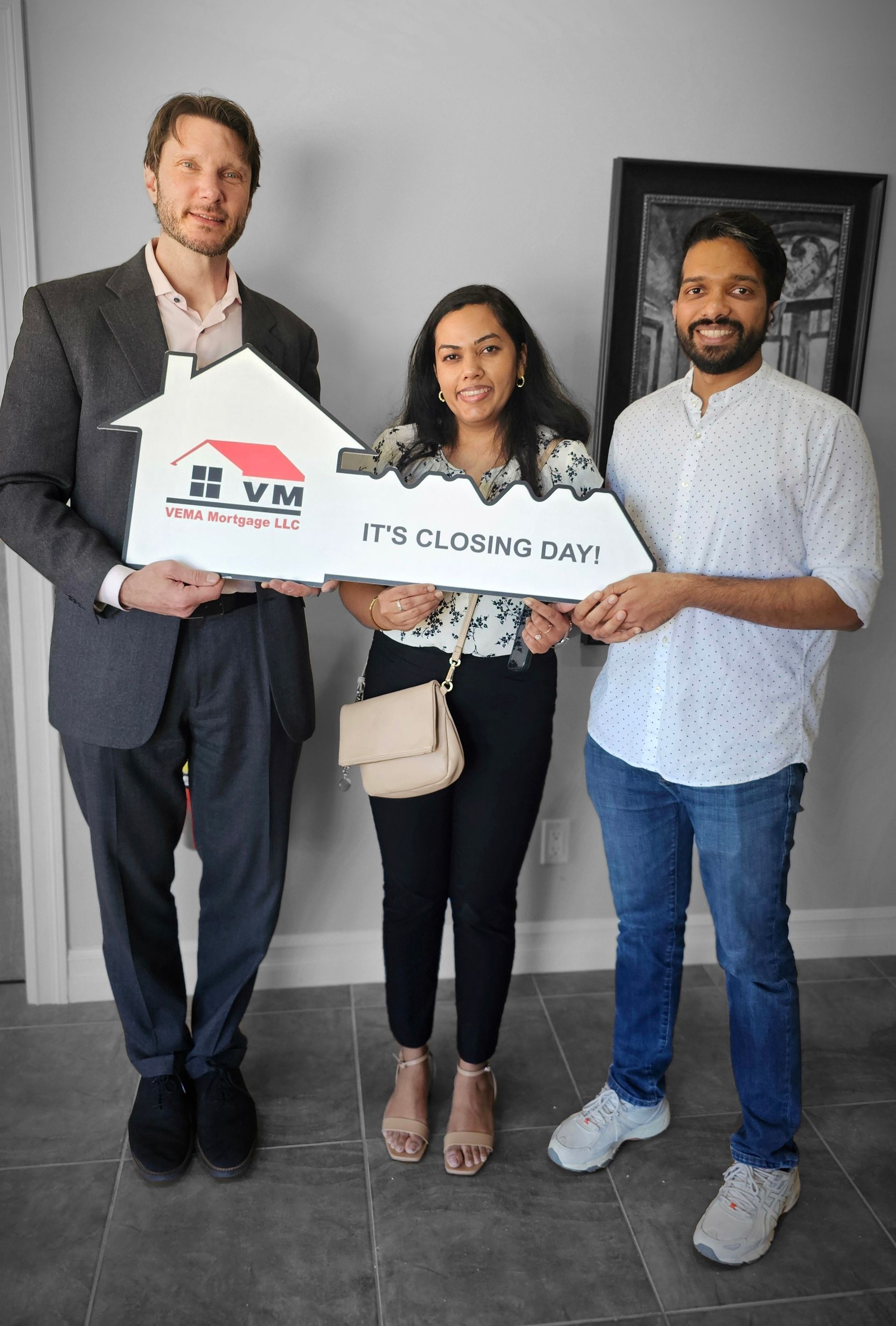 Three people holding a large check in an office, smiling at the camera.