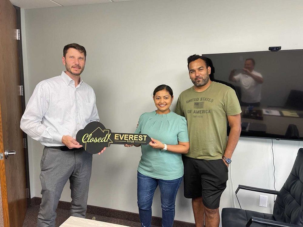 Three people holding a “Glade to Everest” sign in a conference room with a TV on the wall
