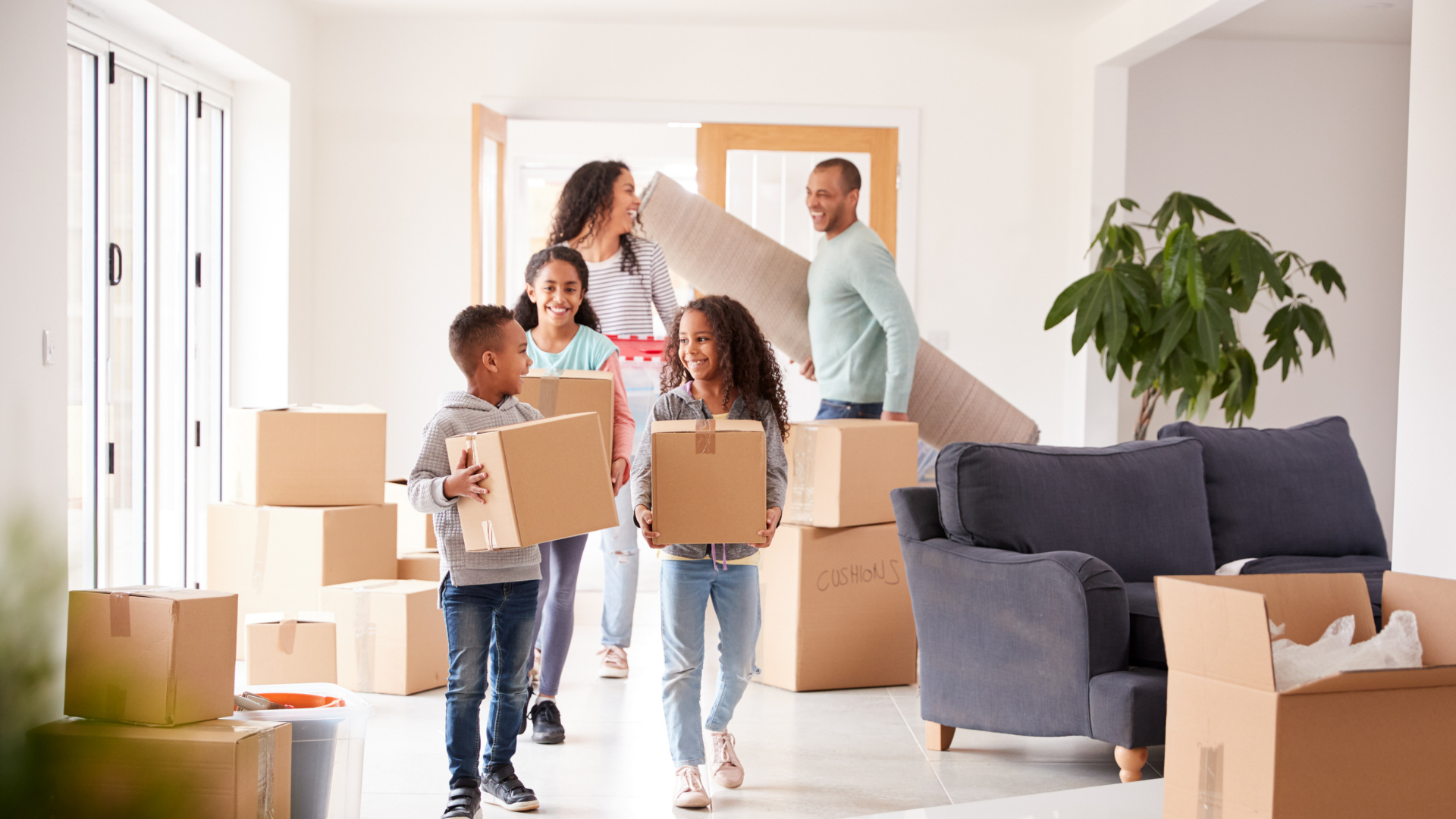 Family carrying boxes into a bright living room during a move