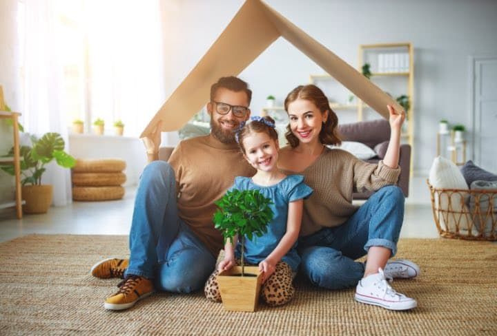 Couple and child sitting on the floor with a small potted plant in a bright living room