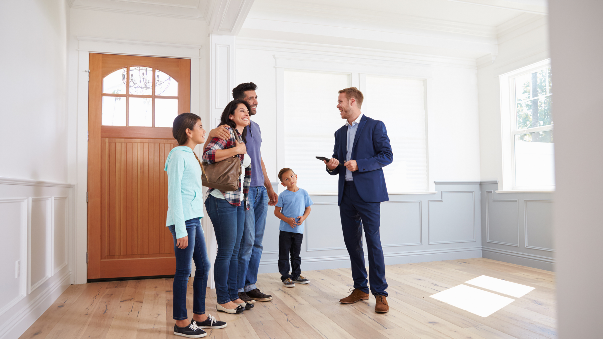 Family and agent talking in a bright, empty house with boxes and a moving blanket