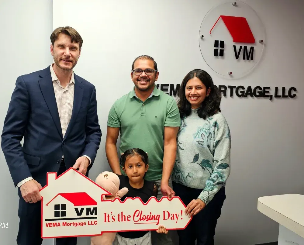 Four people holding a “It’s the Closing Day!” sign in a VM Mortgage office lobby.