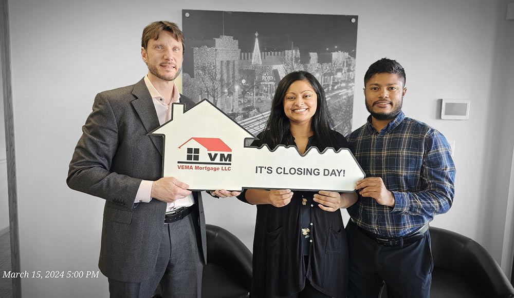 Three people holding a ceremonial key and house-shaped sign in an office setting