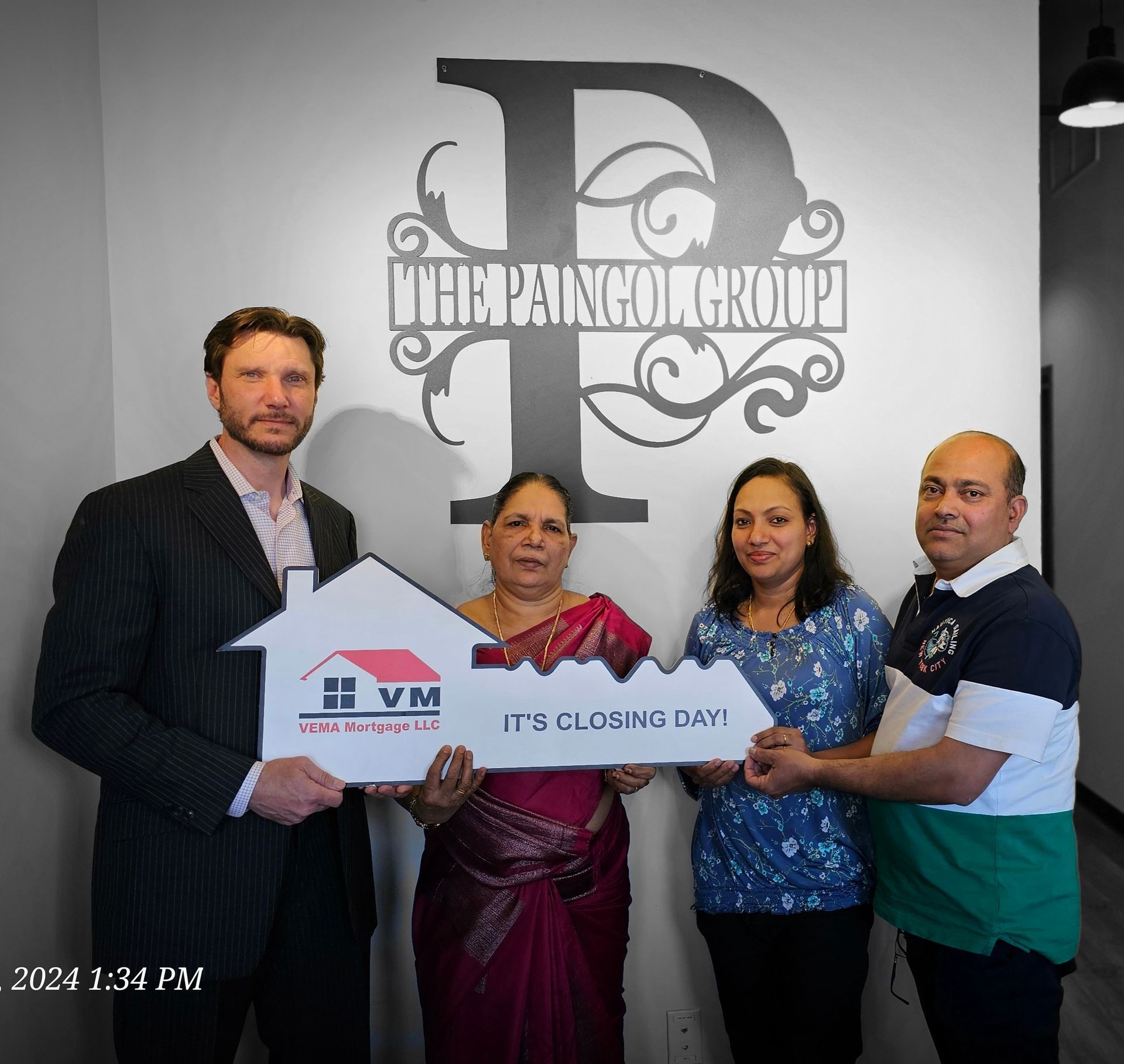 Four people hold a real estate sign in an office with “The Paragon Group” logo on the wall.