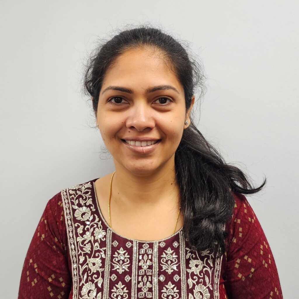 Smiling woman in a maroon patterned top against a plain light background