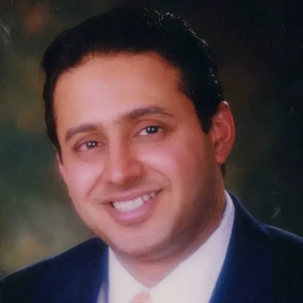 Smiling man in a dark suit and white shirt against a soft blurred background