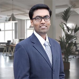 Smiling man in a navy suit and glasses standing in a modern office lobby