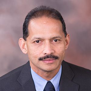 Head-and-shoulders portrait of a man in a dark suit and blue shirt against a neutral background
