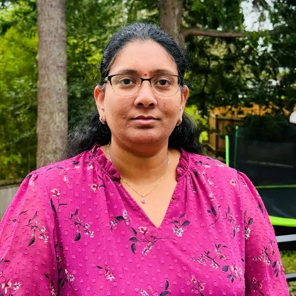 Person wearing glasses and a bright pink top standing outdoors with trees in the background