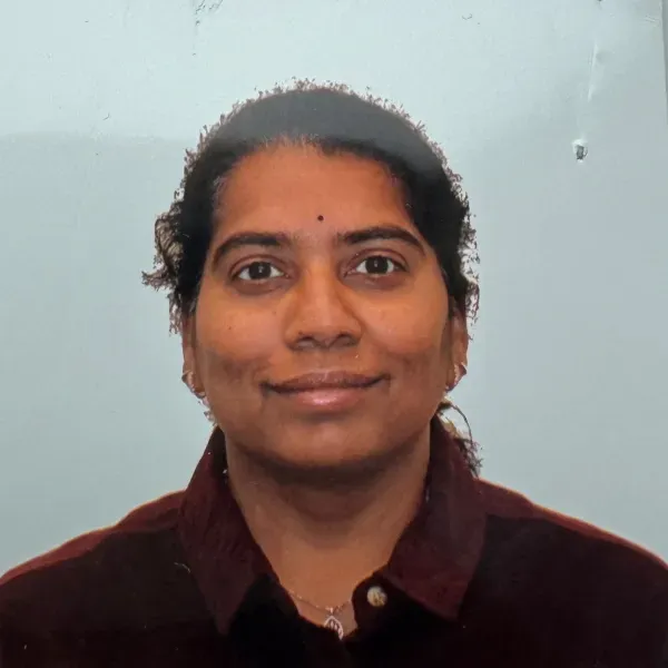 Portrait of a person smiling against a light blue wall, wearing a dark maroon shirt.