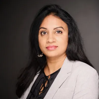 Studio portrait of a woman with long dark hair wearing a light gray blazer and black top against a dark background
