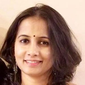 Close-up portrait of a smiling woman with shoulder-length dark hair and a small bindi on her forehead