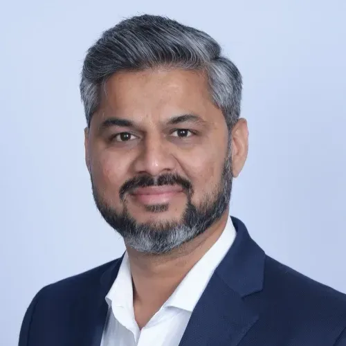 Studio headshot of a smiling man in a navy blazer and white shirt against a light blue background