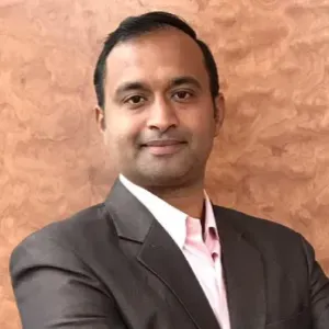 Portrait of a smiling man in a dark suit and pink shirt against a textured tan background