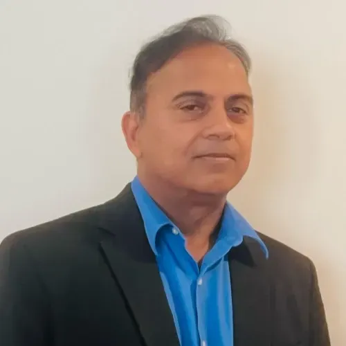 Man in a blue shirt and dark blazer posing against a plain white wall
