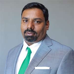 Man in a gray suit with green tie and white shirt, posed against a gray background.
