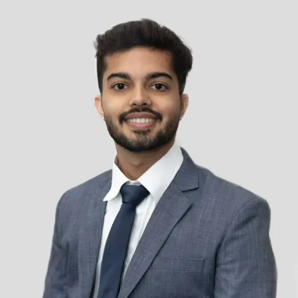 Smiling professional in a gray suit, white shirt, and navy tie against a light background.