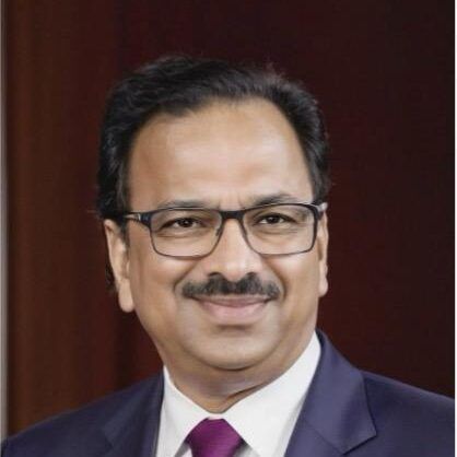 Portrait of a man in glasses and a purple suit, smiling against a dark background