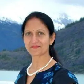 Woman wearing a pearl necklace, standing outdoors with mountains and water in the background