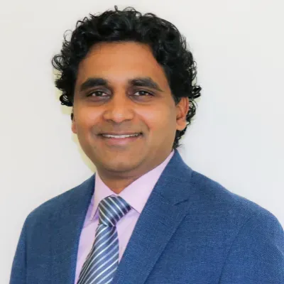 Portrait of a smiling person in a blue blazer and striped tie against a white background