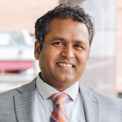 Smiling man in a gray suit and striped tie, posed indoors against a softly blurred background