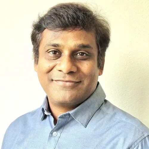 Portrait of a smiling person in a light blue shirt against a plain beige background