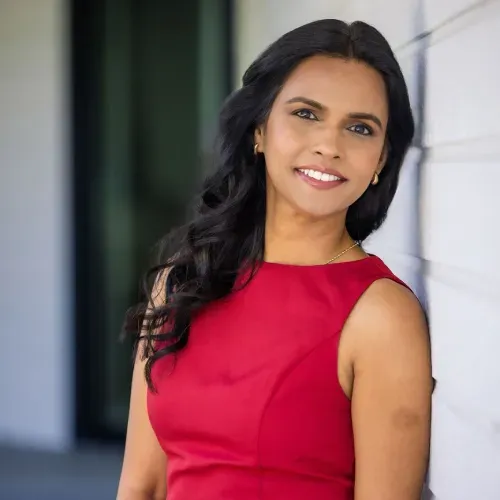 Smiling woman in a red sleeveless dress standing indoors near a doorway