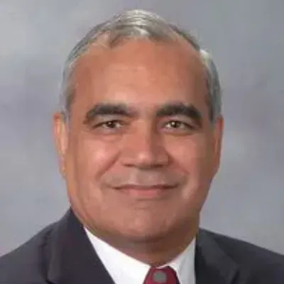 Studio headshot of a smiling man in a dark suit and red tie against a gray background