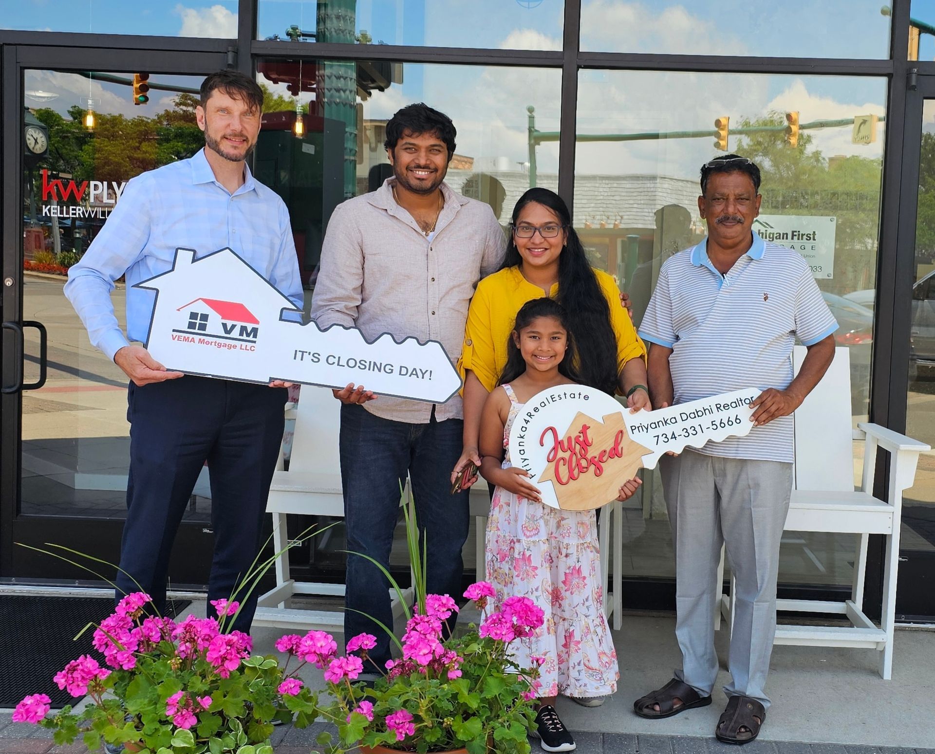 Five people posing outdoors, holding oversized keys and a heart-shaped sign in front of a storefront.
