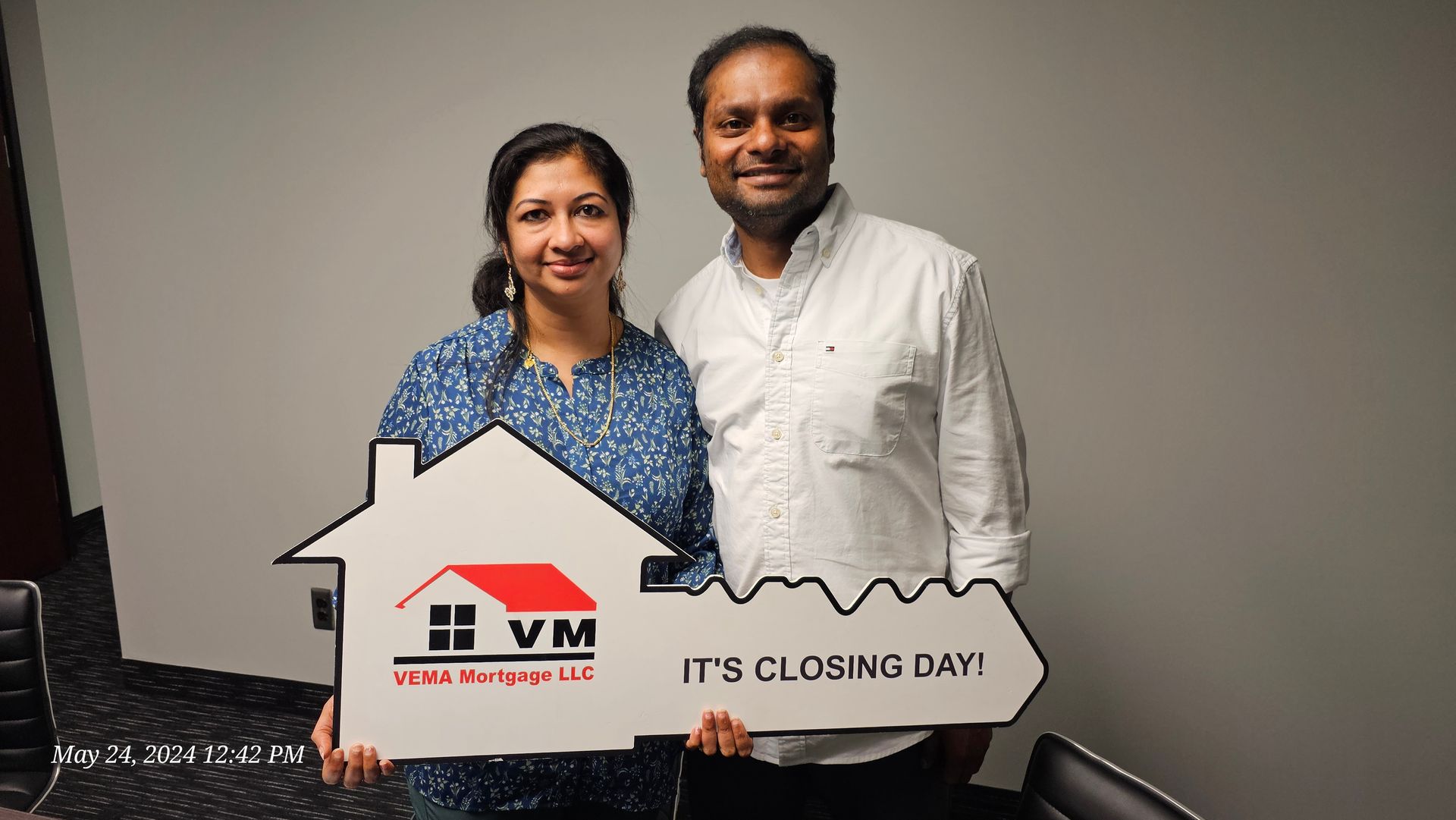 Two people posing indoors holding a house-shaped sign reading “IT’S CLOSING DAY!”