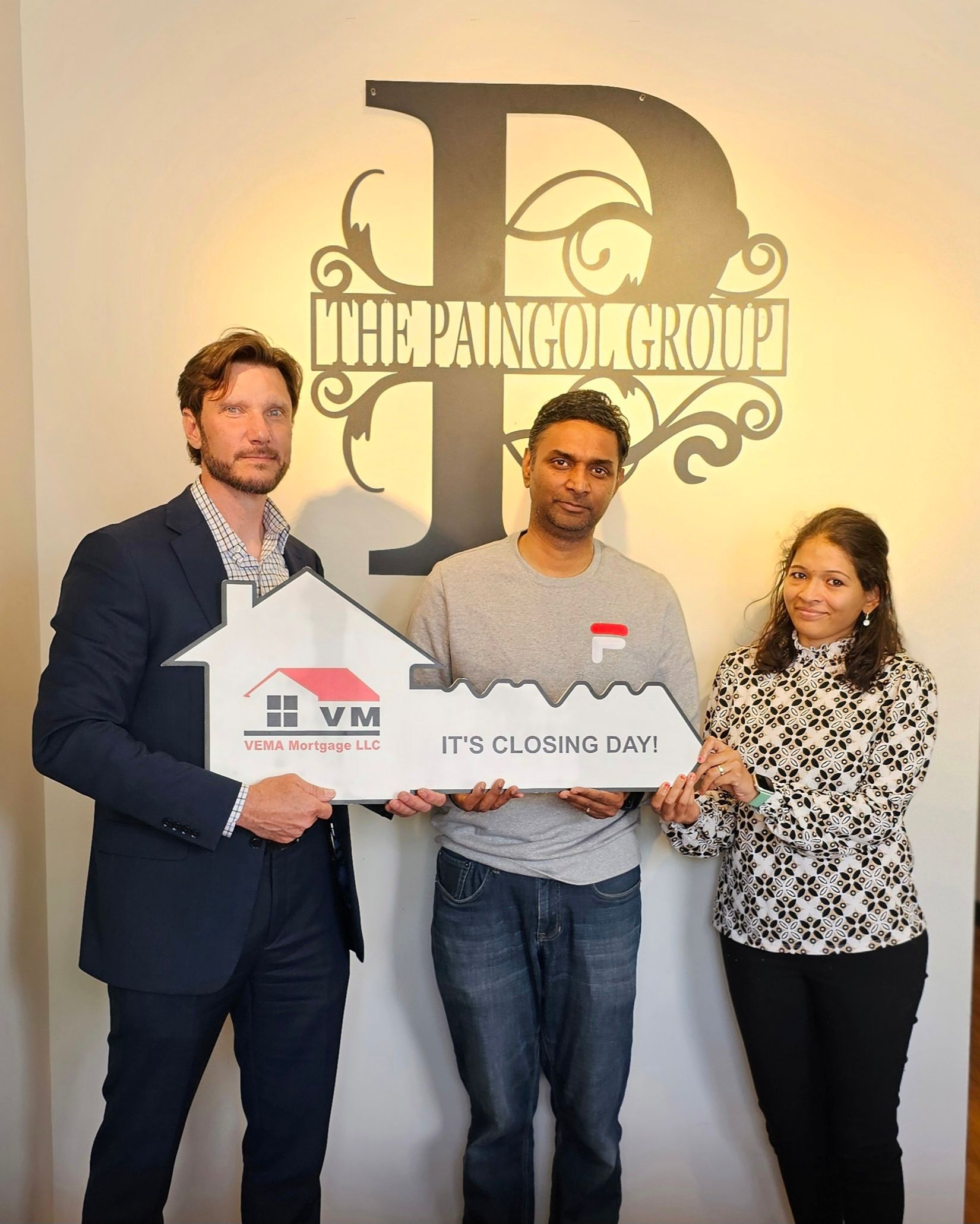 Three people holding a large check in front of a wall logo, smiling in an office lobby.