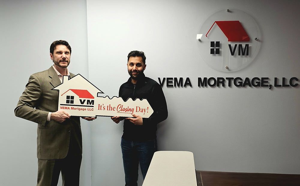 Two men holding a VEMA Mortgage sign in an office lobby.