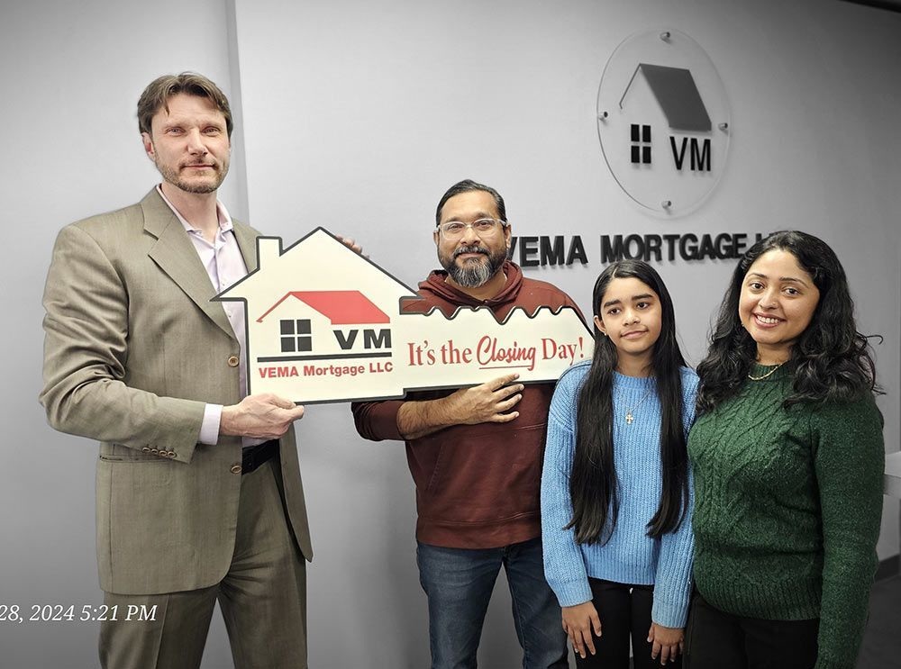 Four people posing indoors with a large house-shaped sign for WEMA Mortgage.
