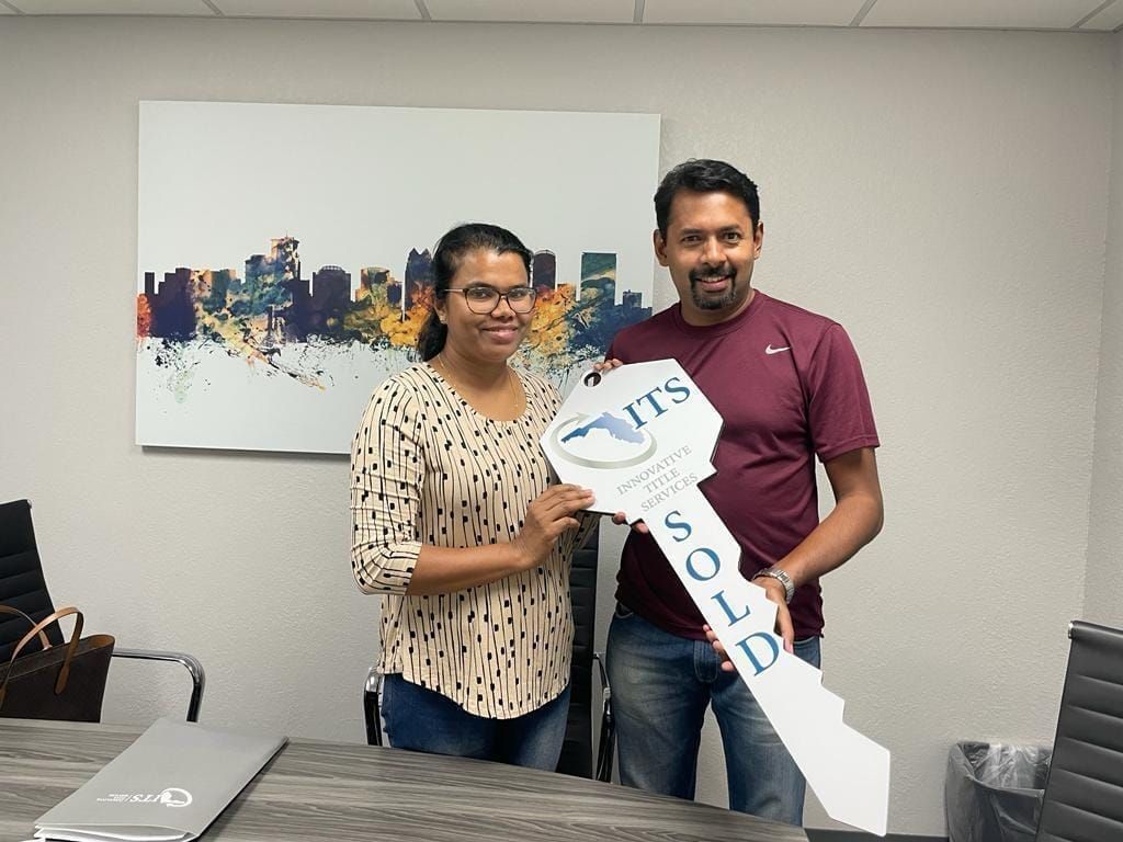 Two people smiling and holding a large white “Sales” arrow sign in an office.