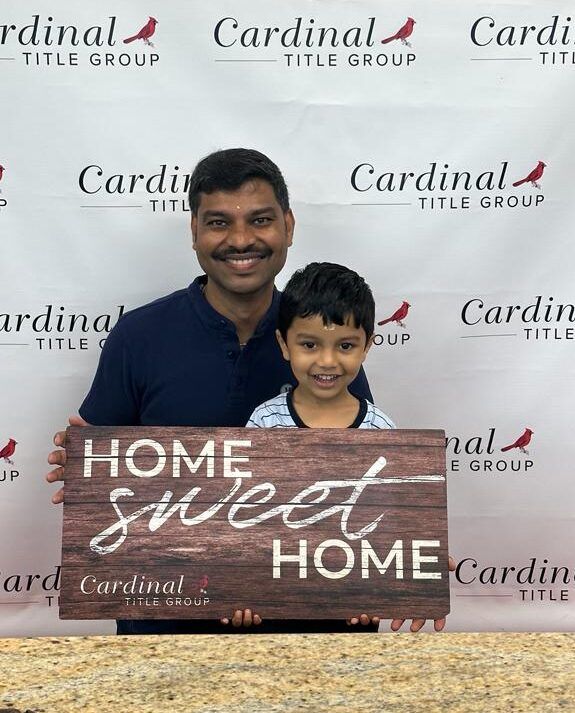 Man and child holding a “Home Sweet Home” sign in front of a Cardinal Title Group backdrop