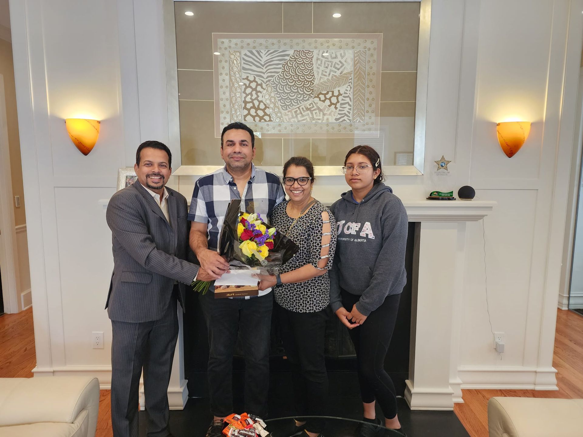 Four people smiling and holding a bouquet in a bright indoor lobby.