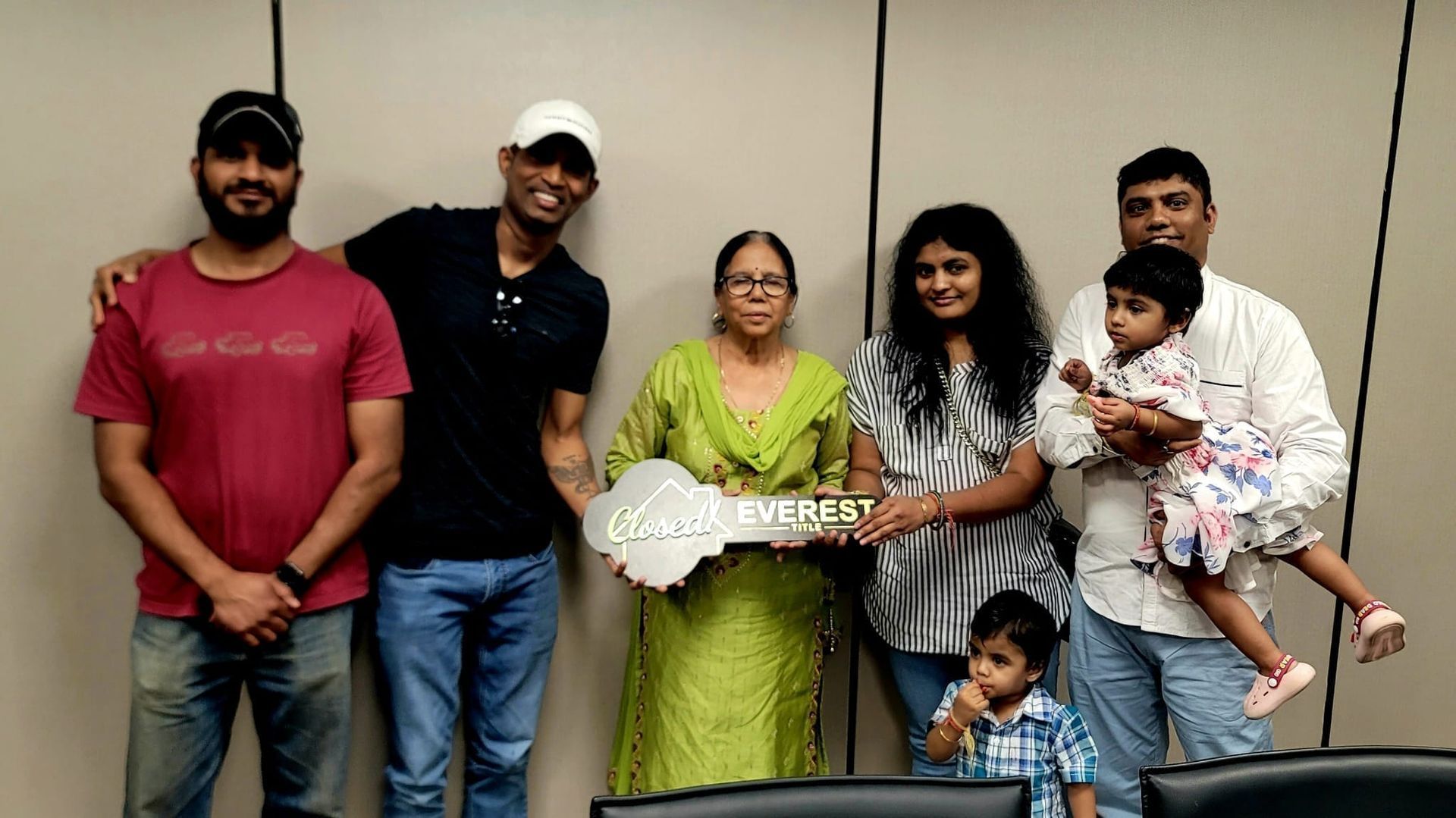 Six people pose indoors around a flower arrangement and a small child being held.
